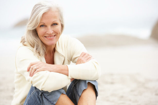 Older woman sitting on beach and smiling