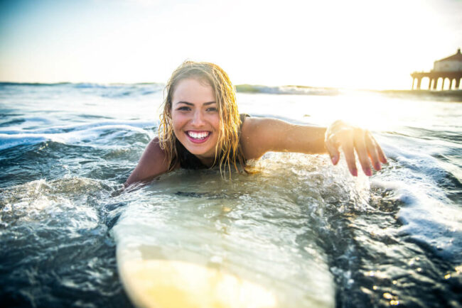 Young woman on surfboard in the ocean with sun setting