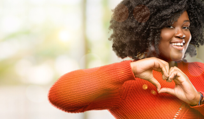 Woman in orange sweater making a heart with her hands